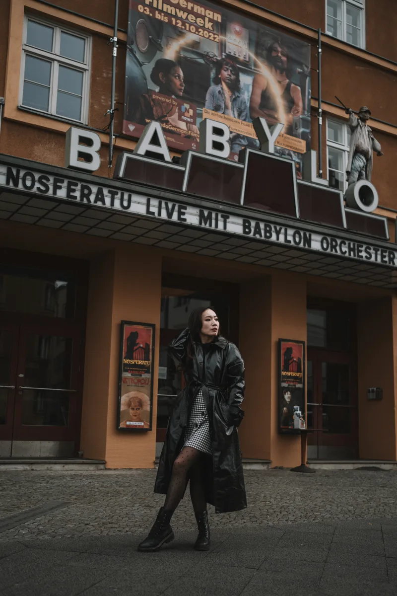 Woman in black jacket and red plaid skirt at vintage cinema with neon signage