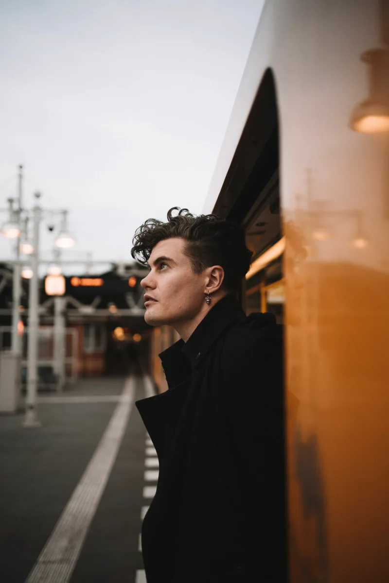 Man in black clothing standing on rooftop at dusk with urban lights