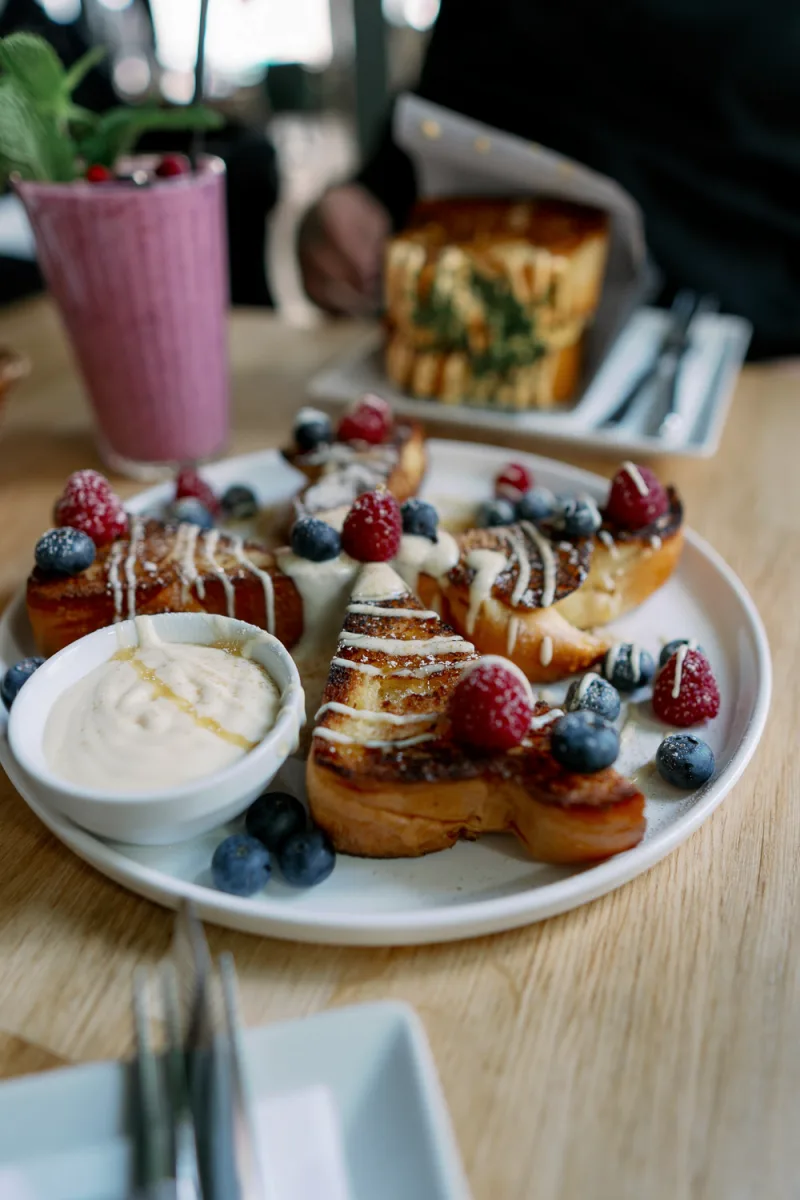 Gourmet pastries with berries and cream sauce arranged on white plate with smoothie