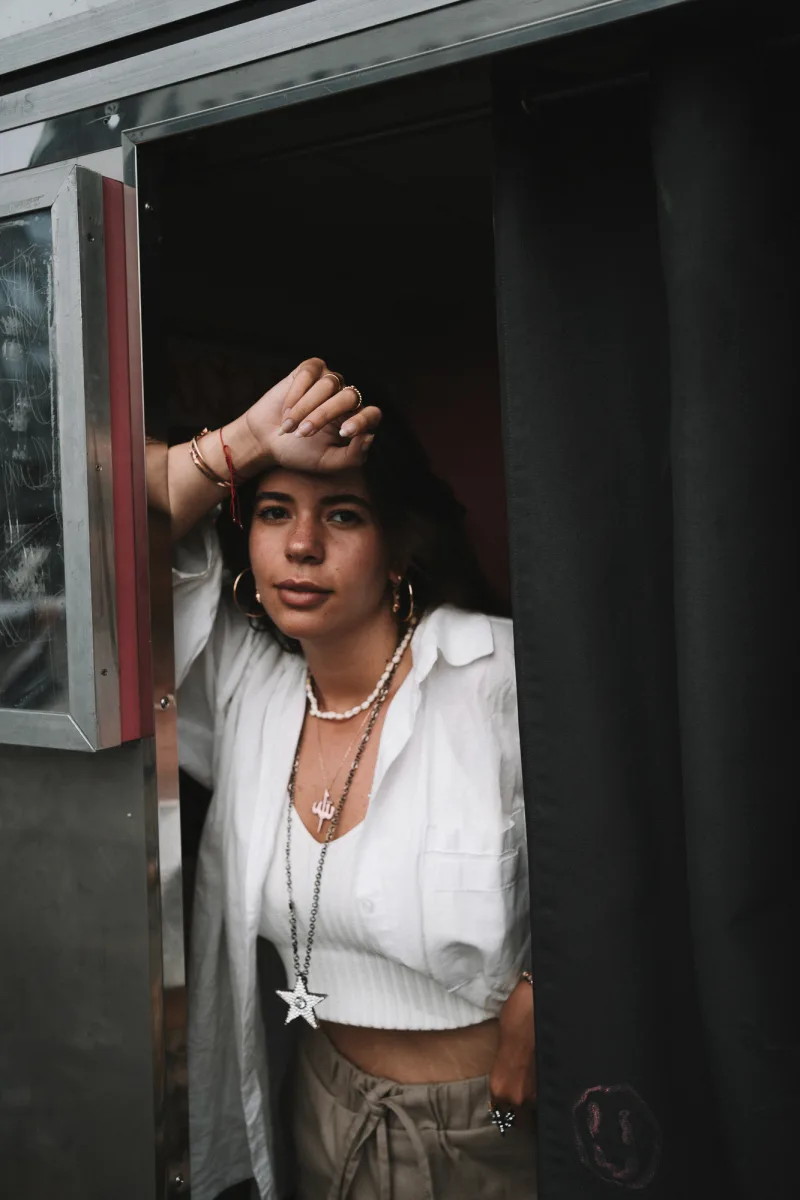 Woman in white shirt reaching toward dark doorway with hand to head