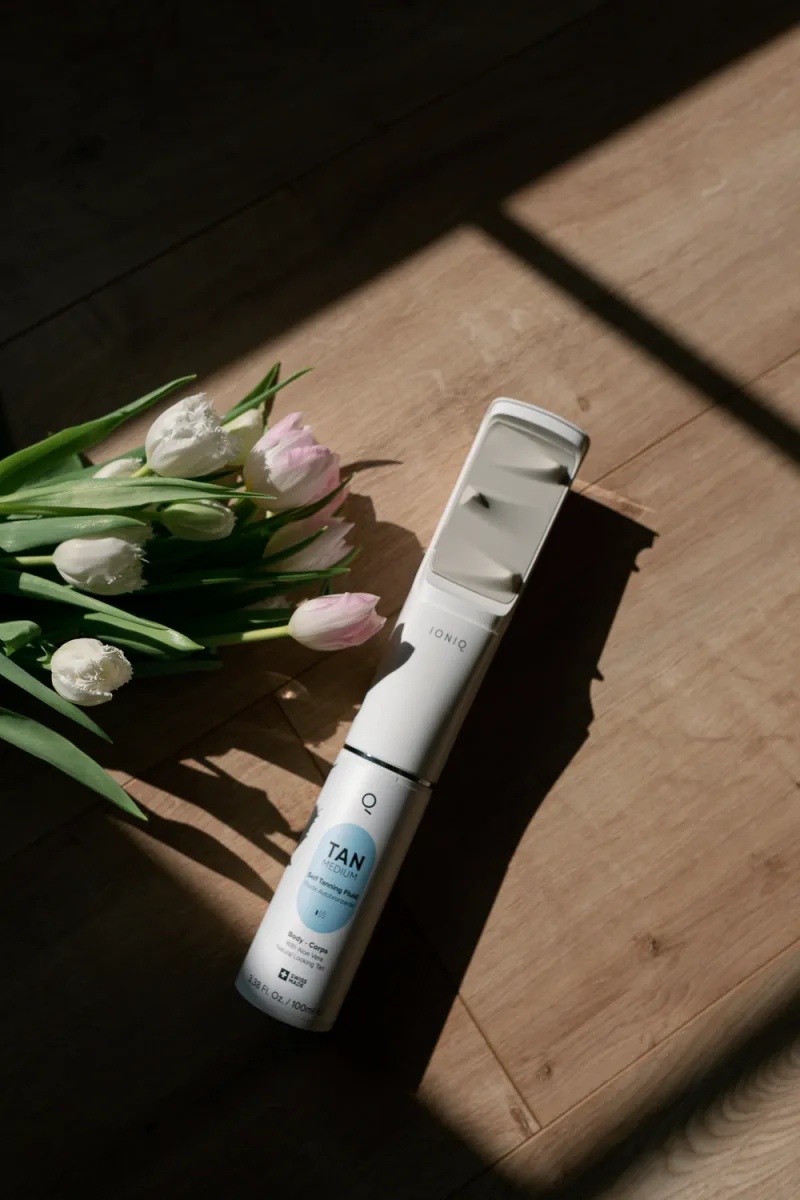 White cosmetic spray bottle next to pink and white tulip flowers