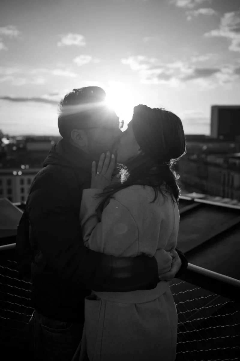 Couple kissing on rooftop silhouetted against cityscape in black and white