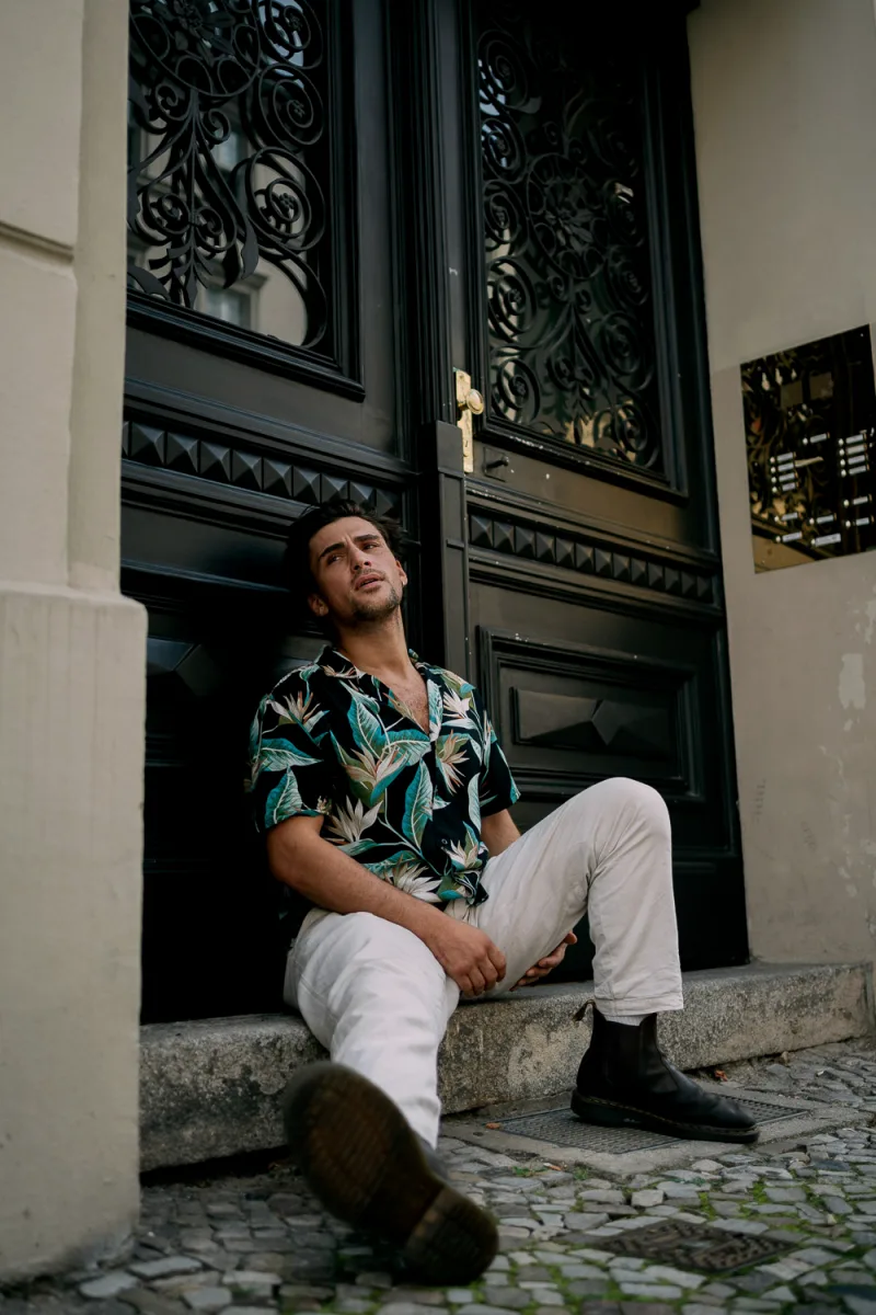 Man in tropical print shirt sitting against ornate black door with architectural details