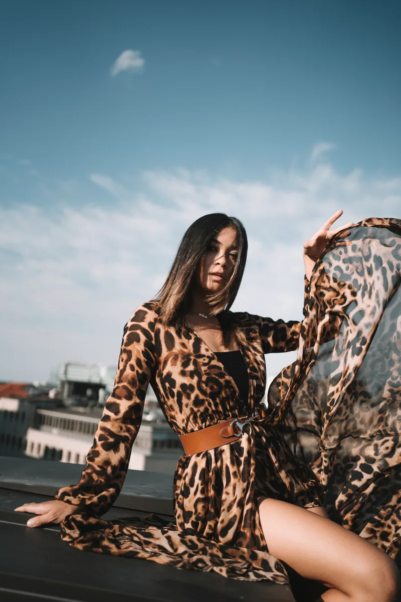 Woman in leopard print dress raising arm on rooftop with clear blue sky