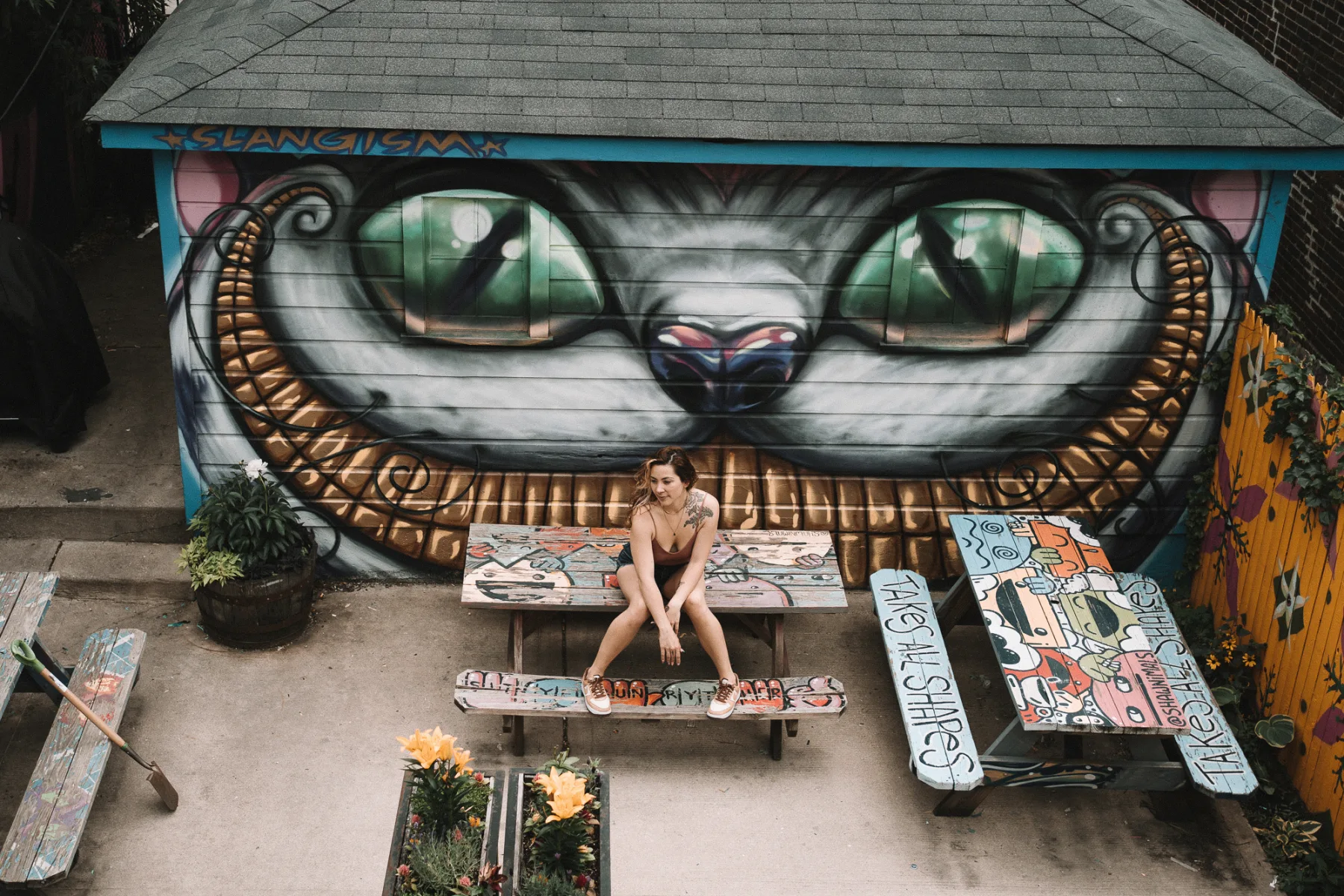 Woman seated on bench against large geometric eye street art mural