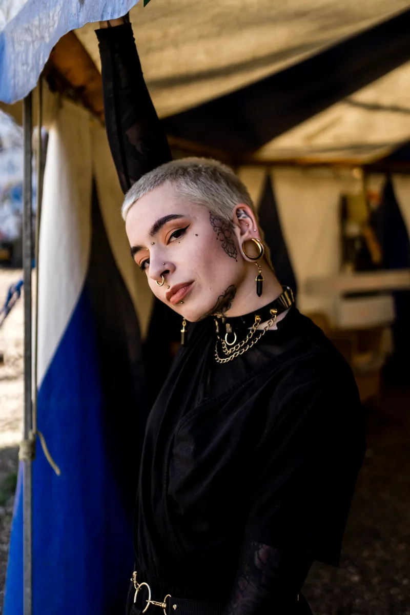 Person with shaved head, gold eye makeup and gold chain jewelry outdoors