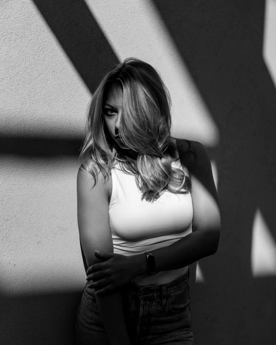 Woman with long hair in white top and black pants with dramatic shadows