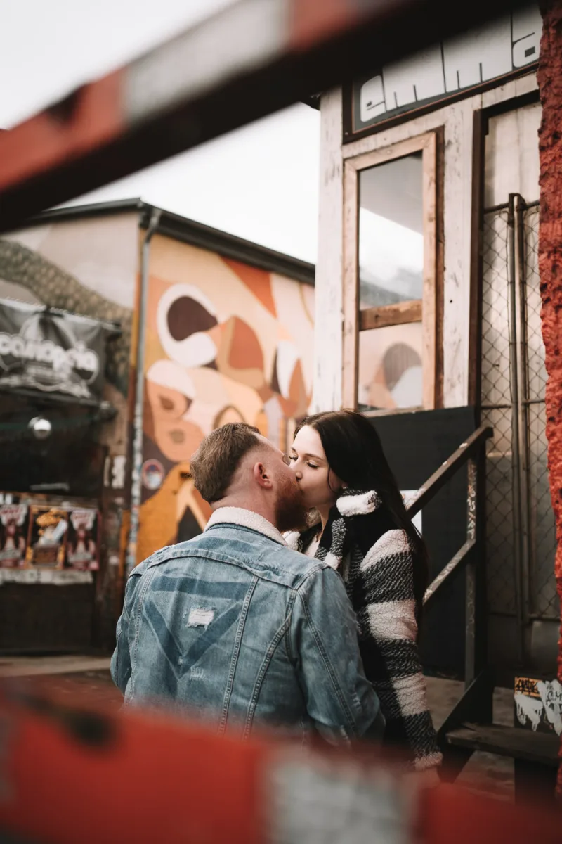 Couple kissing passionately against urban wall with colorful graffiti and metal structures