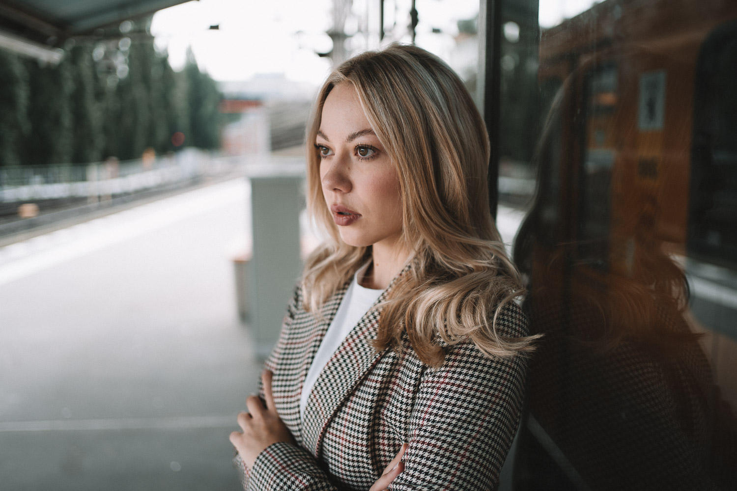 Woman with blonde wavy hair in black houndstooth blazer at train station