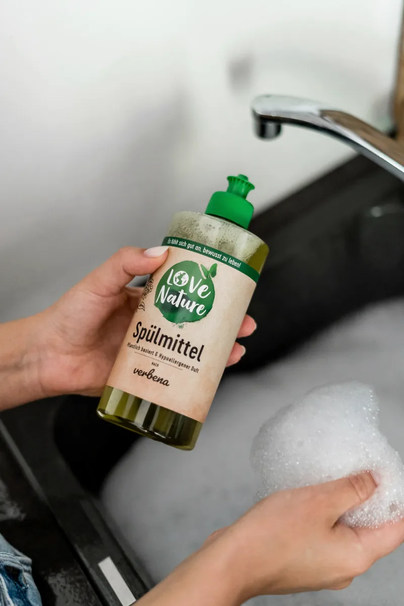 Hands holding natural cleaning product bottle above bathroom sink with soap foam