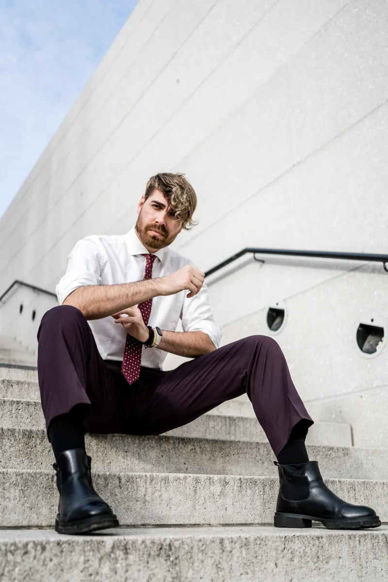 Man in white shirt with burgundy tie sitting on concrete against white building