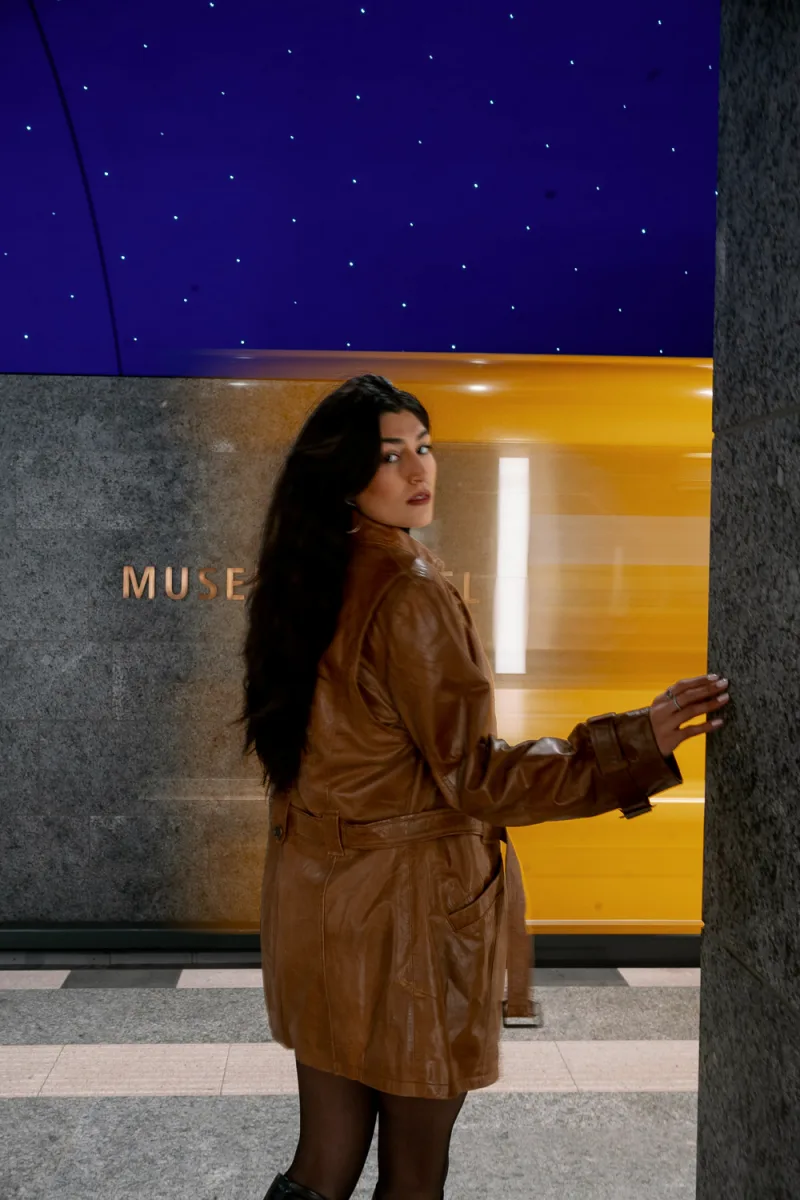 Woman in brown leather jacket looking over shoulder against starlit night sky backdrop