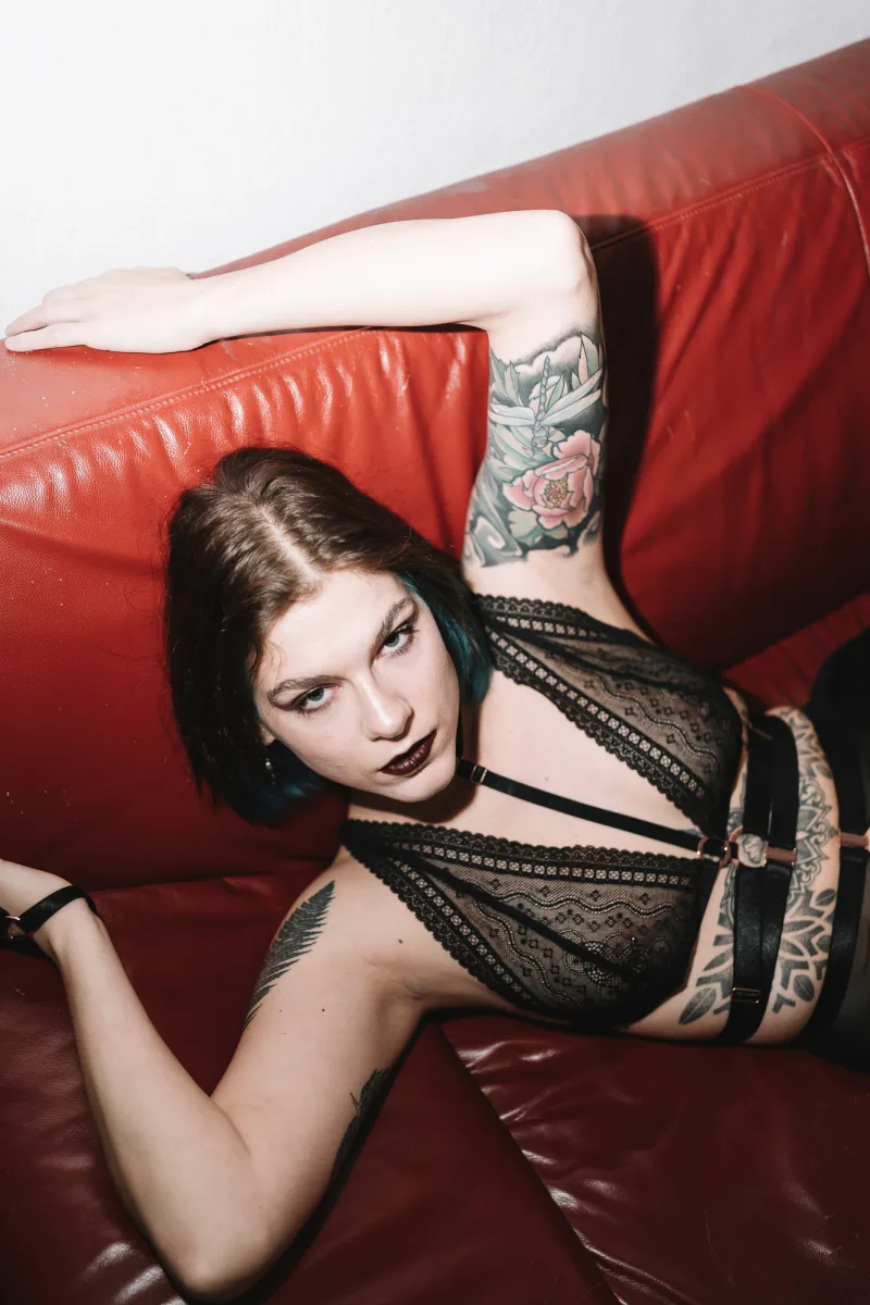 Woman with dark hair on red leather couch wearing black lace lingerie