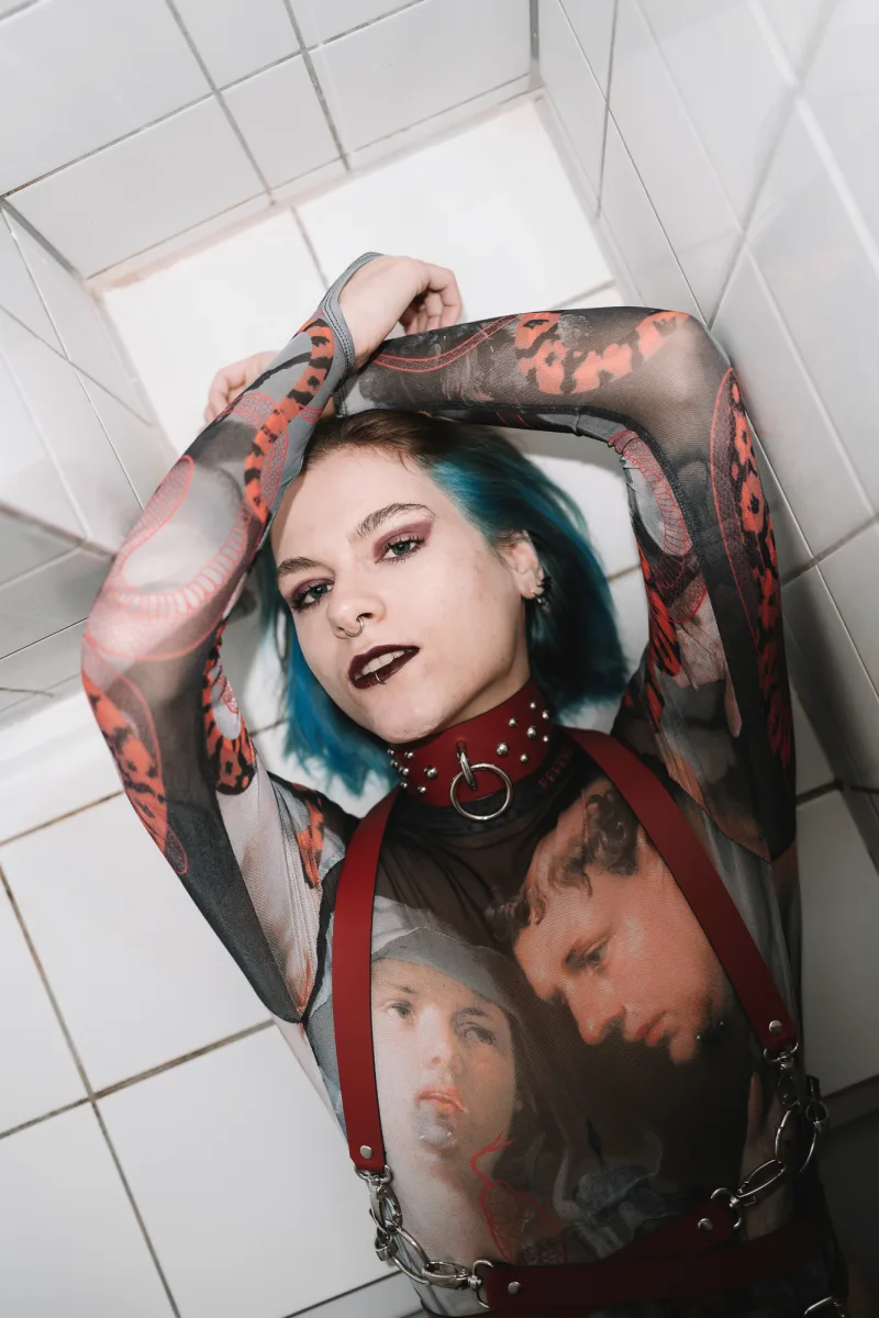 Woman with blue-tinted dark hair holding graphic band merchandise under tiled ceiling