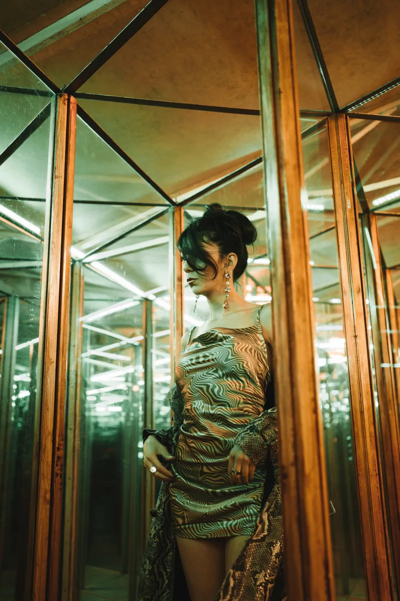 Woman in green and black patterned dress standing in mirrored geometric elevator space
