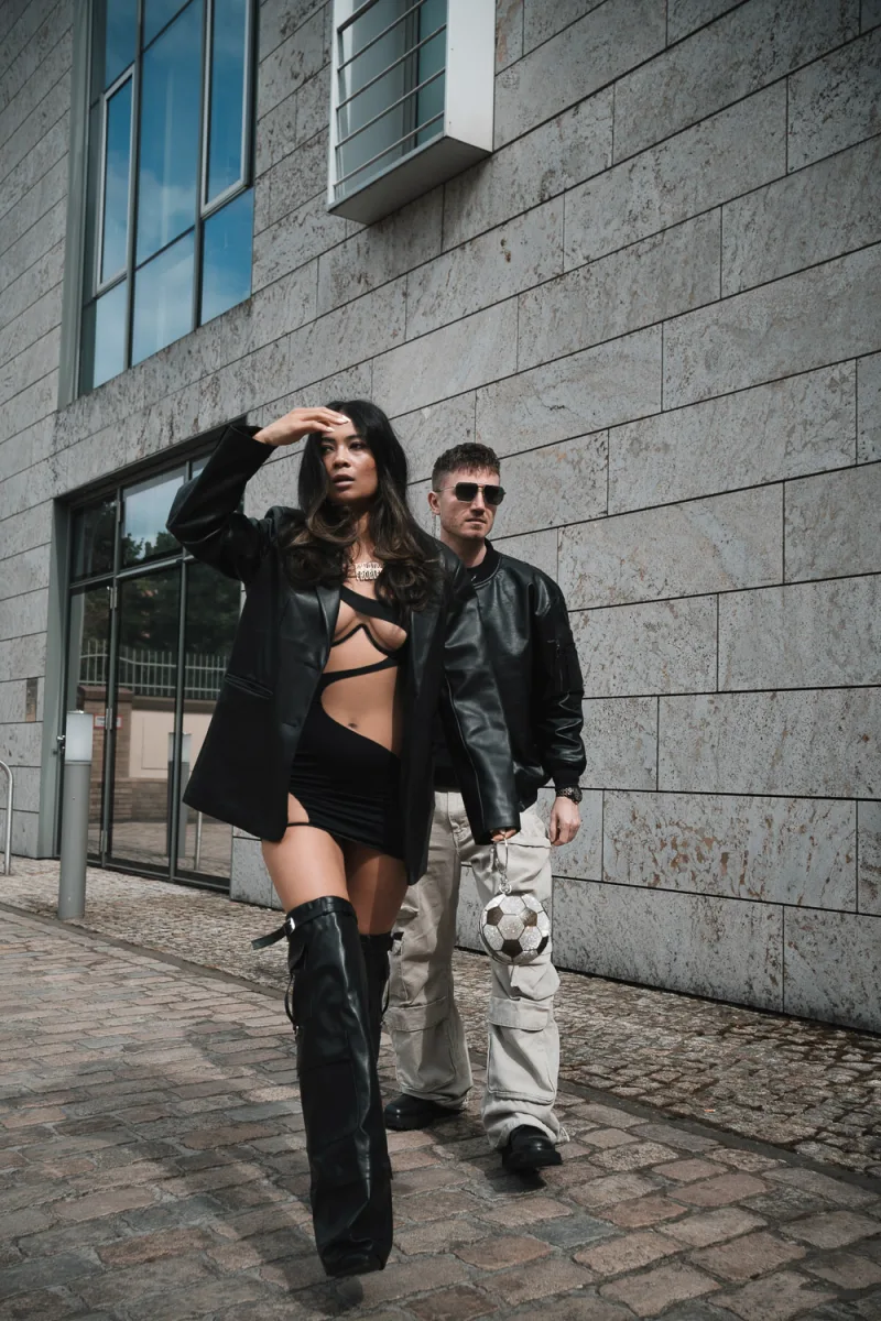 Woman in black outfit with hand to forehead walking beside man outdoors
