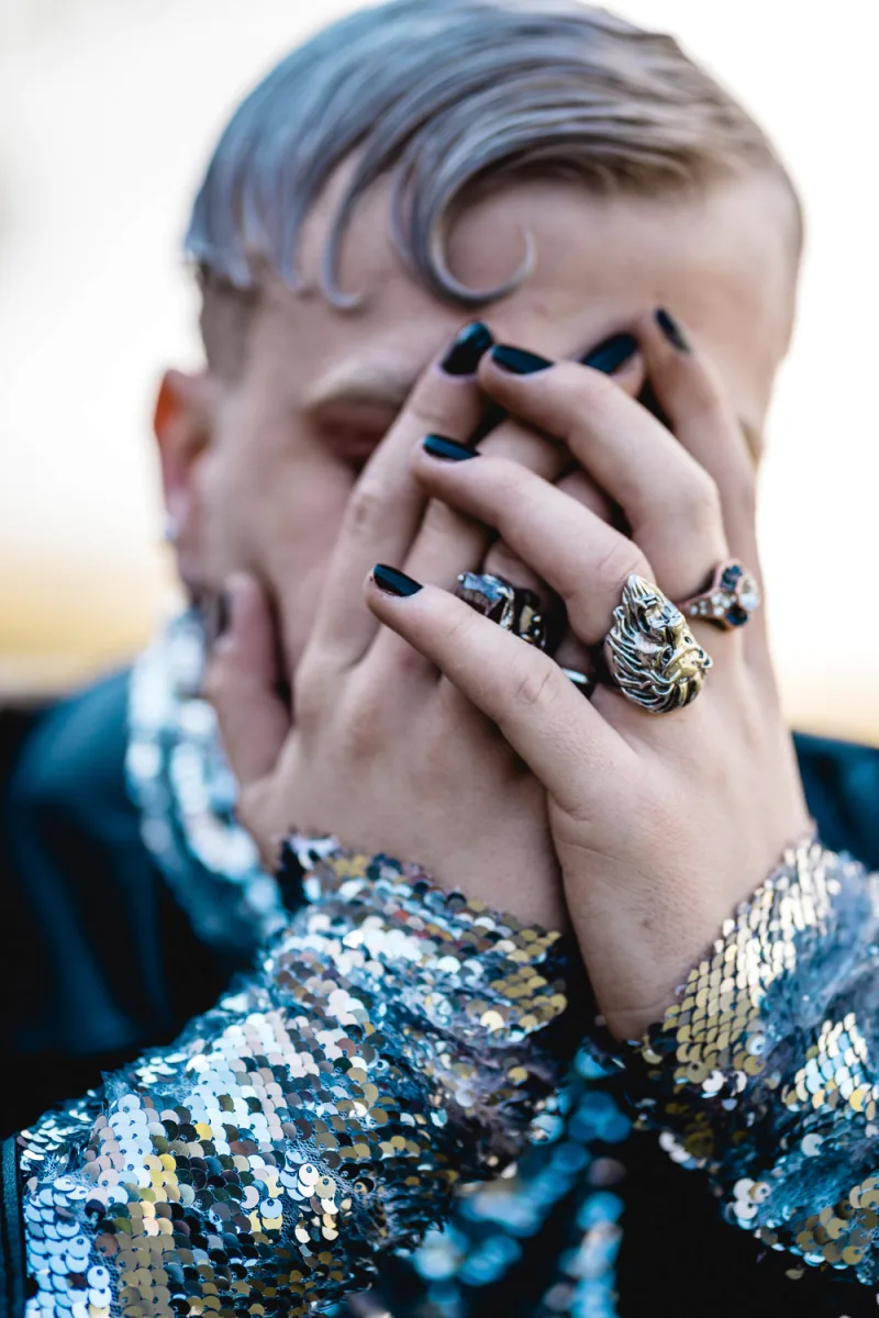 Person with blue and gold sequined jacket and elaborate hand jewelry close-up