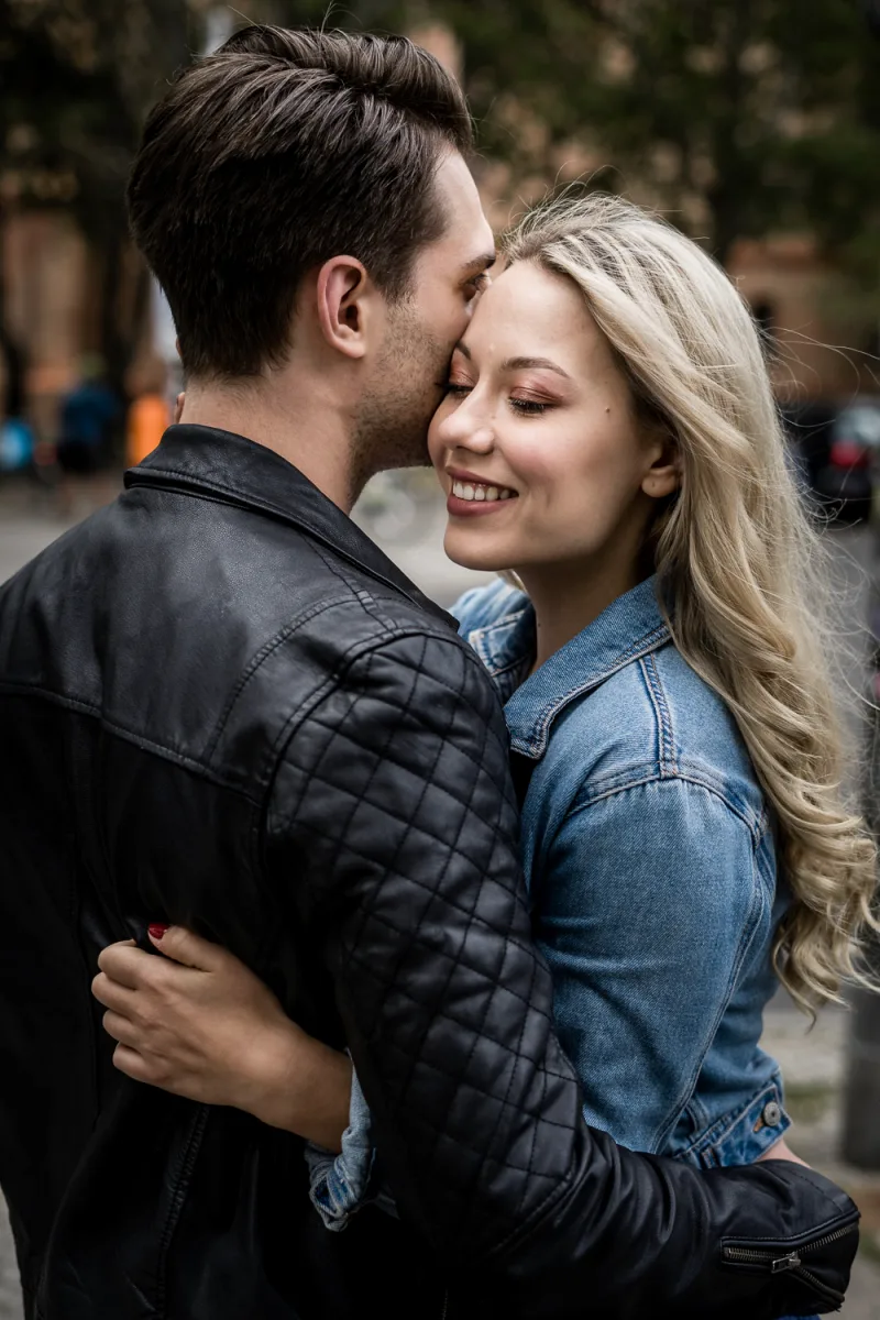 Couple kissing outdoors, man in quilted black jacket, woman in denim jacket, urban