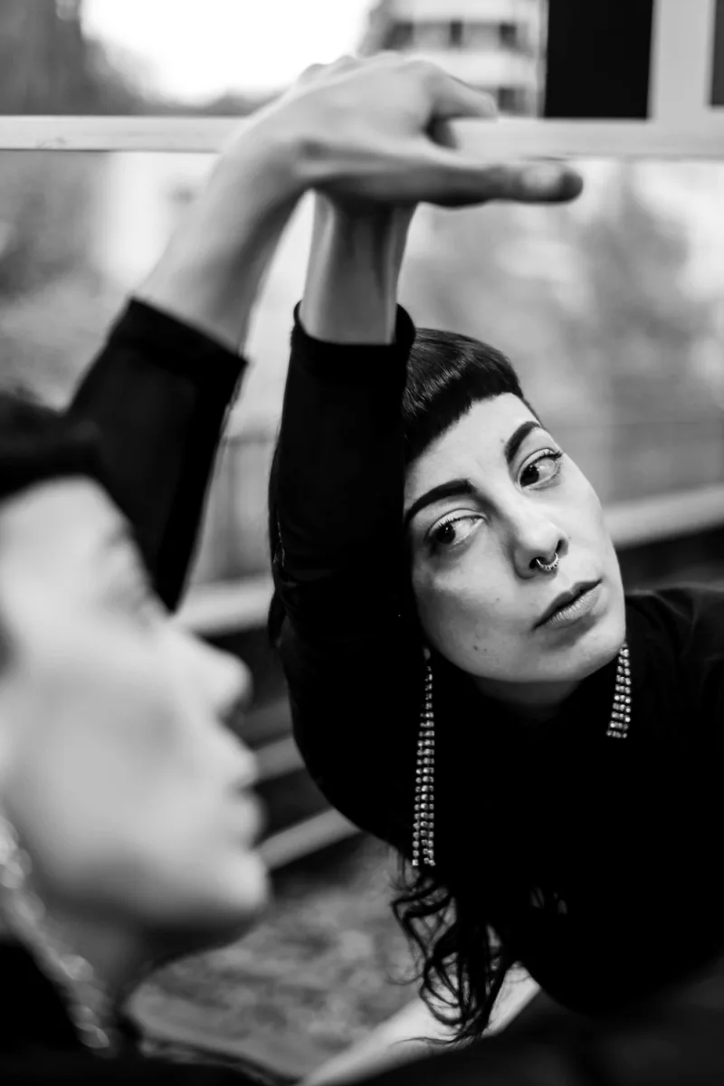 Woman with short dark bob and nose piercing hand above head black and white