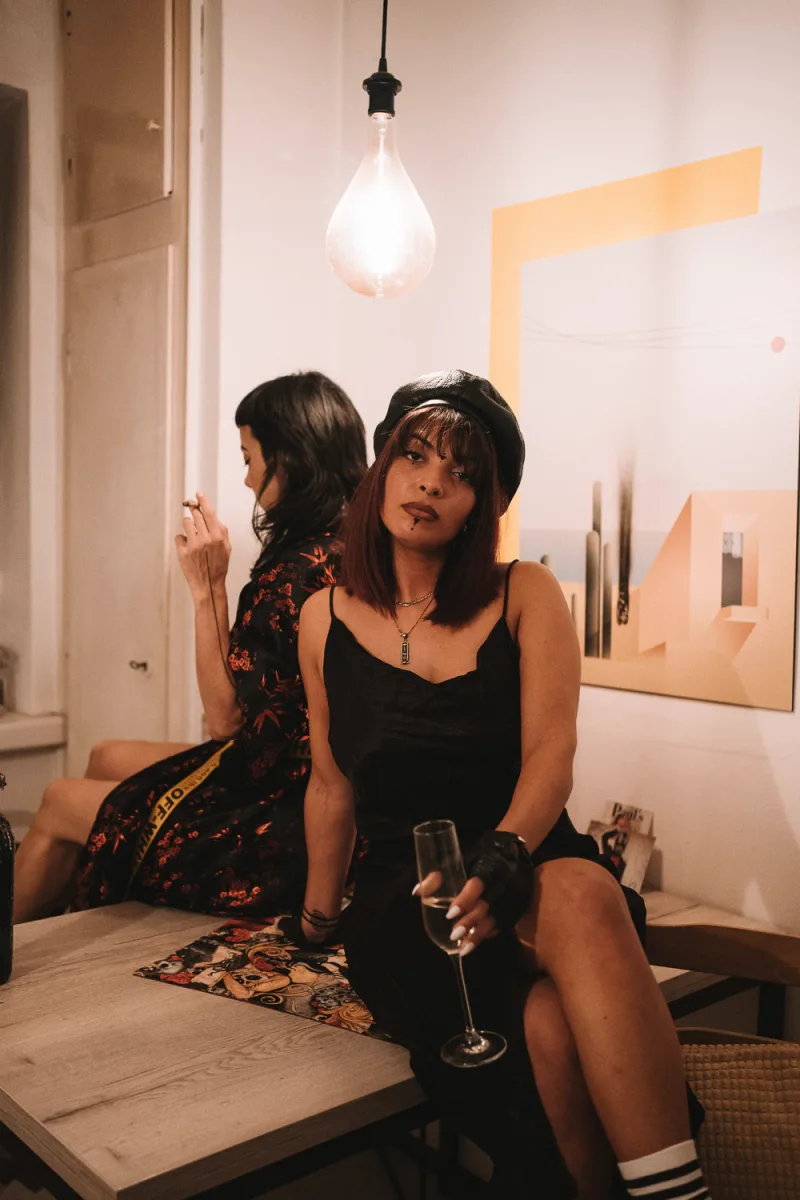 Two women in casual attire in warm interior with one holding wine glass