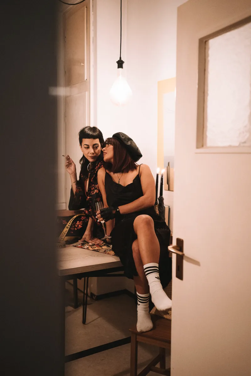 Two women in white minimalist room one in black one in patterned vest