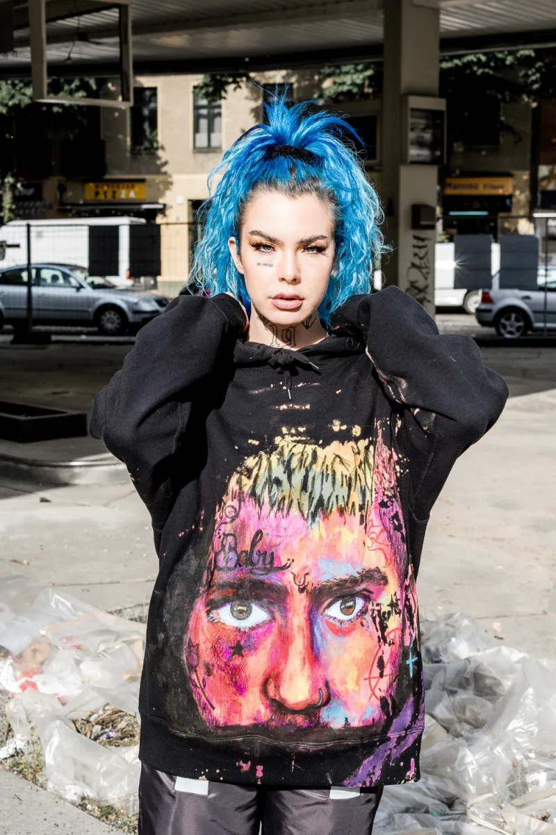 Person with vibrant bright blue hair in destroyed graphic hoodie posing outdoors