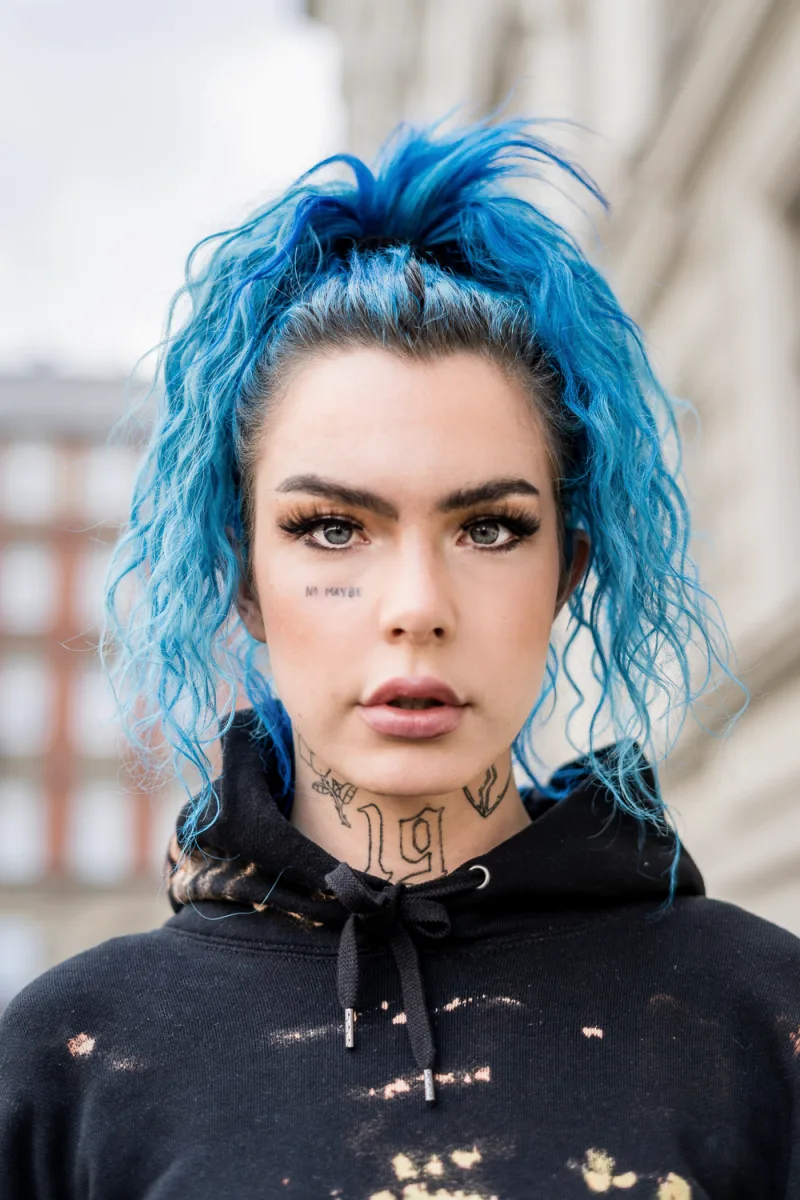 Woman with vibrant cyan hair in top knot bun, neck tattoos, dark clothing