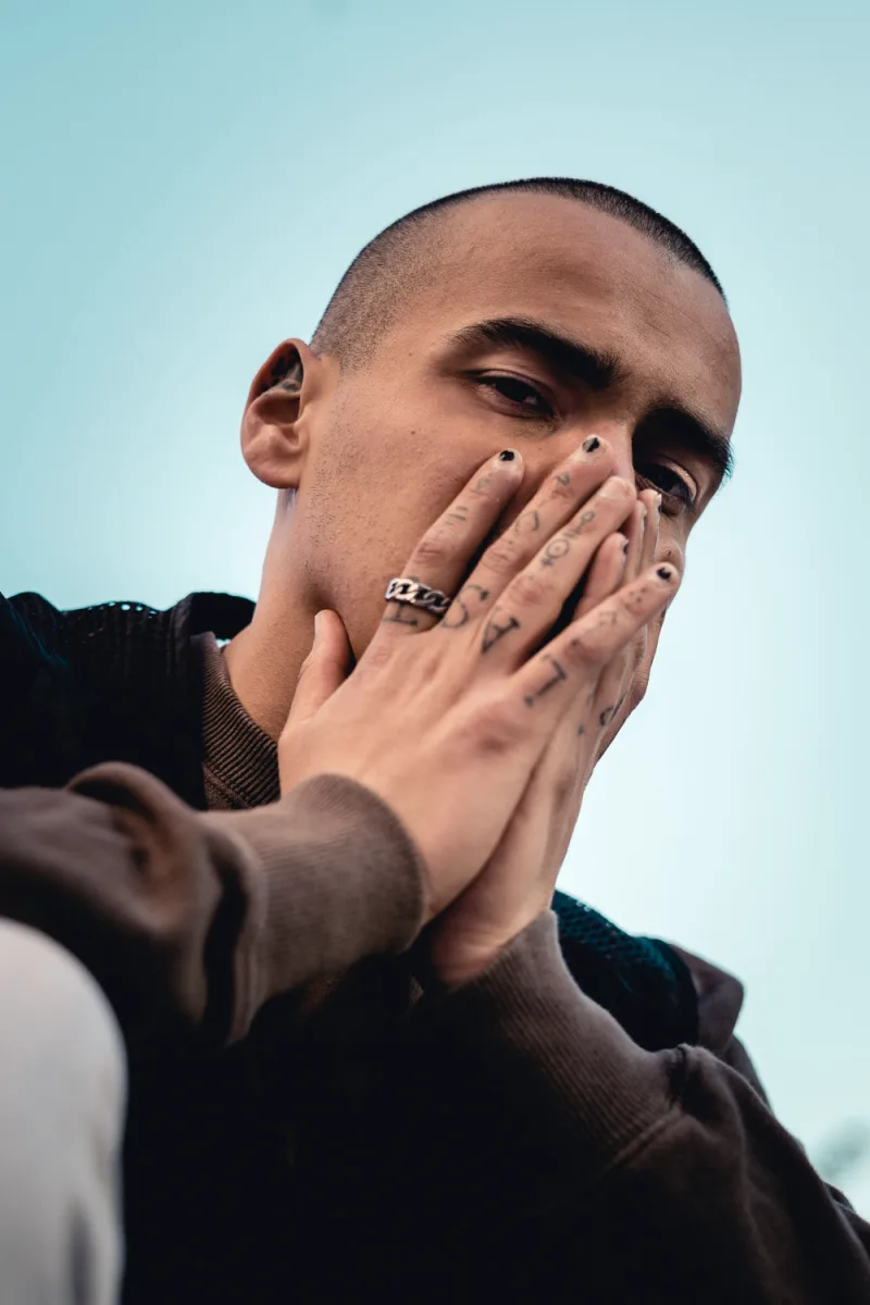 Man in textured dark sweater and blue turtleneck leaning against light surface