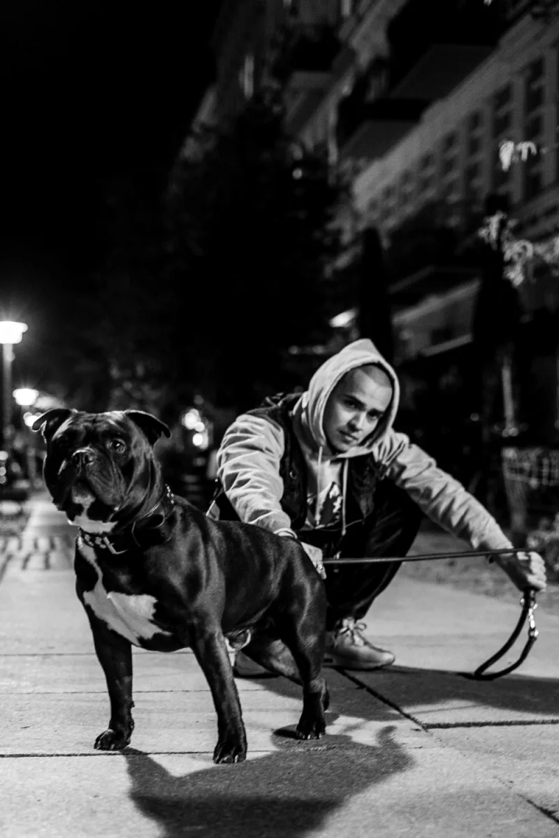 Woman in light hoodie walking dark dog at night on city street black and white
