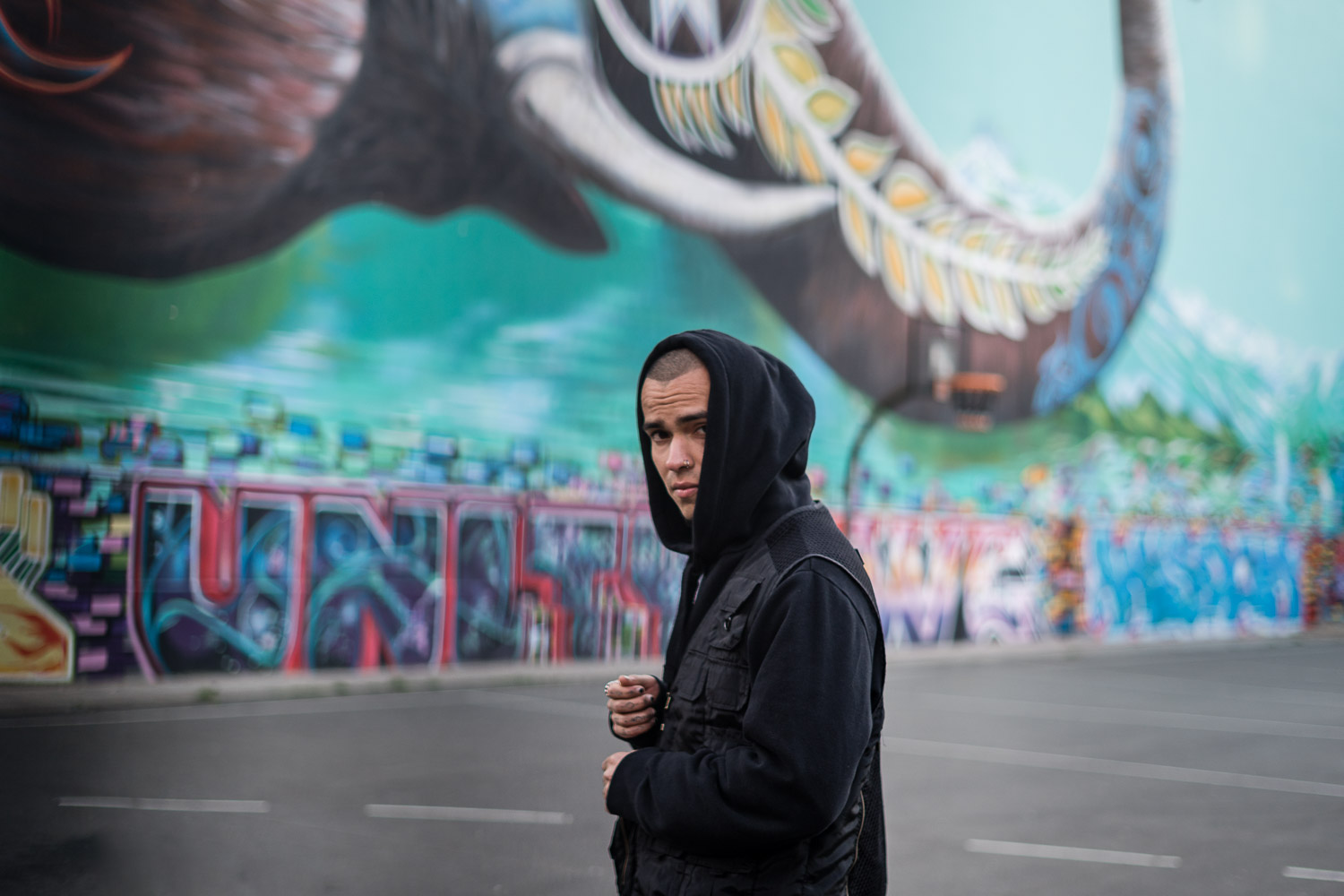 Man in black hoodie standing before large vibrant street art mural
