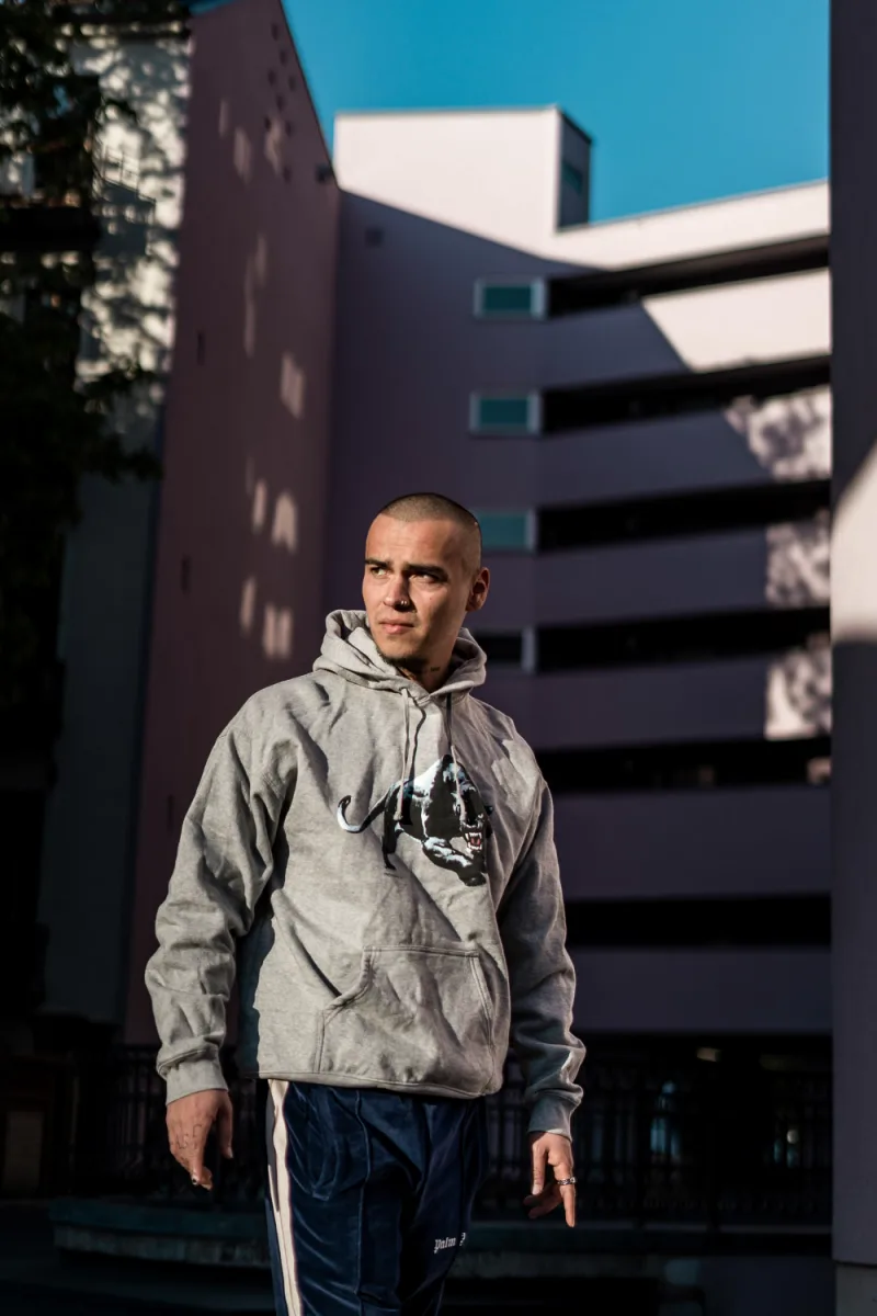 Man with shaved head in grey hoodie and navy track pants outdoors