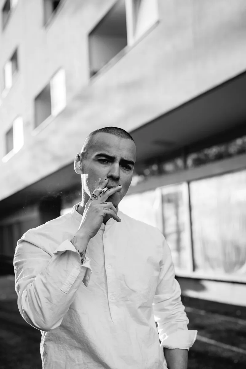 Man in white button shirt smoking cigarette under concrete brutalist architecture