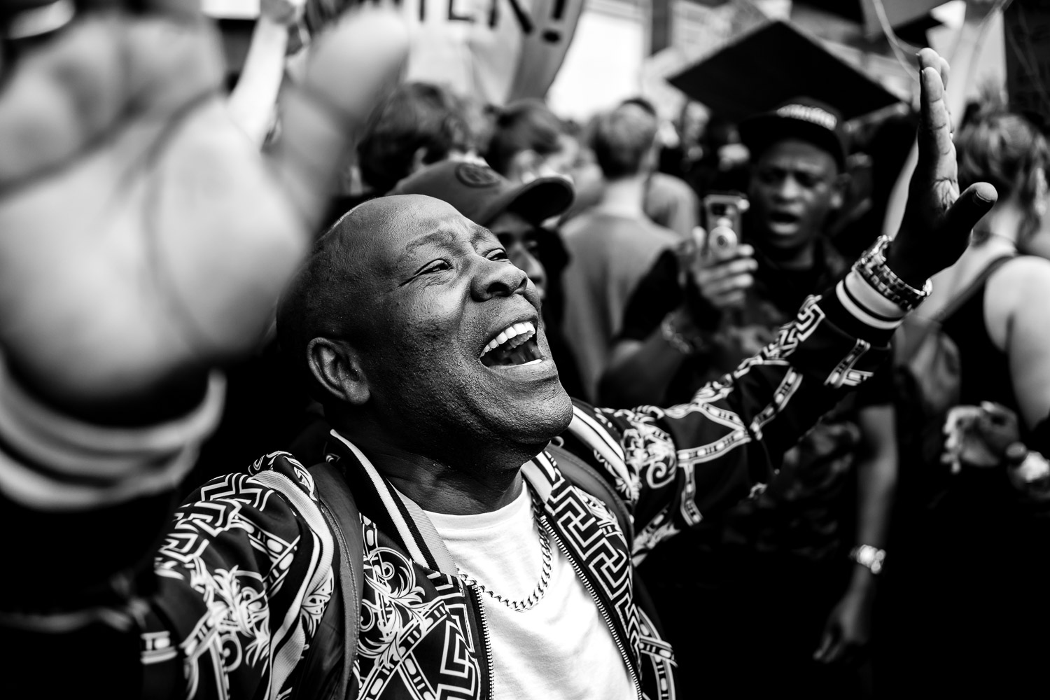 Man with raised arm at outdoor gathering wearing geometric patterned jacket