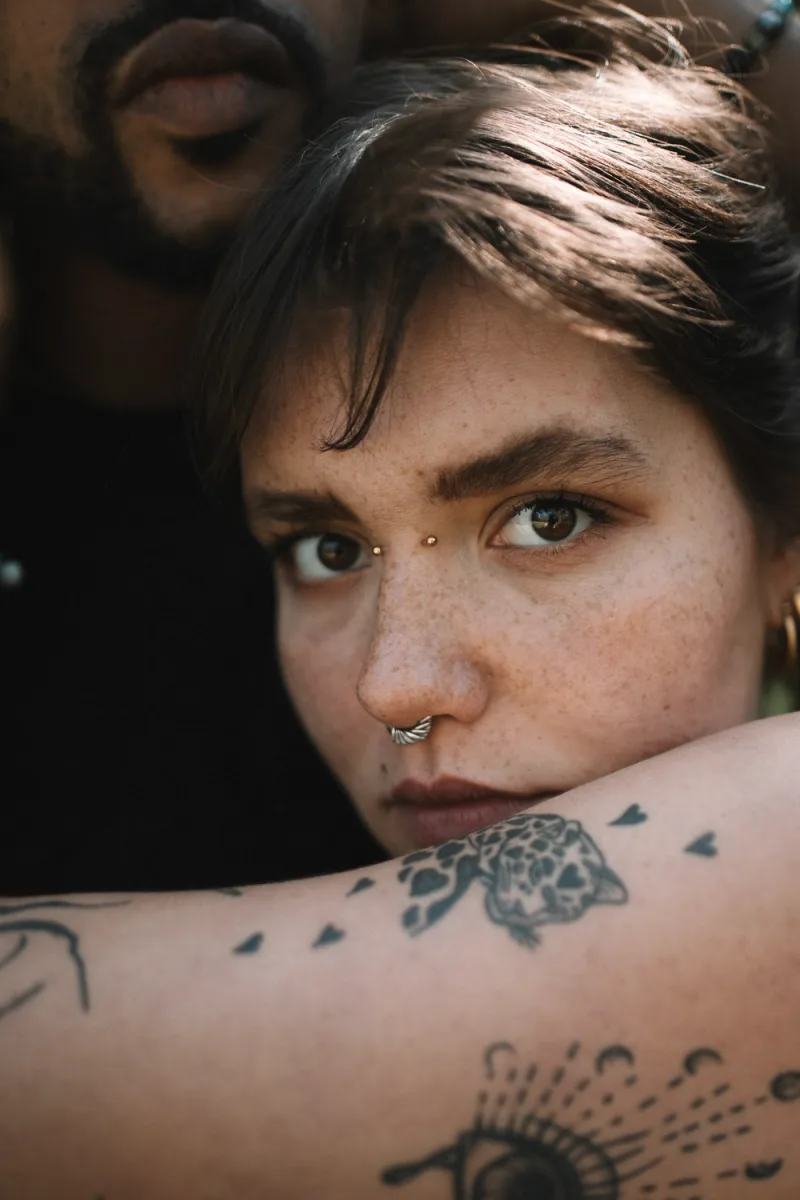 Person with freckles and nose piercing gazing to side with visible arm tattoo