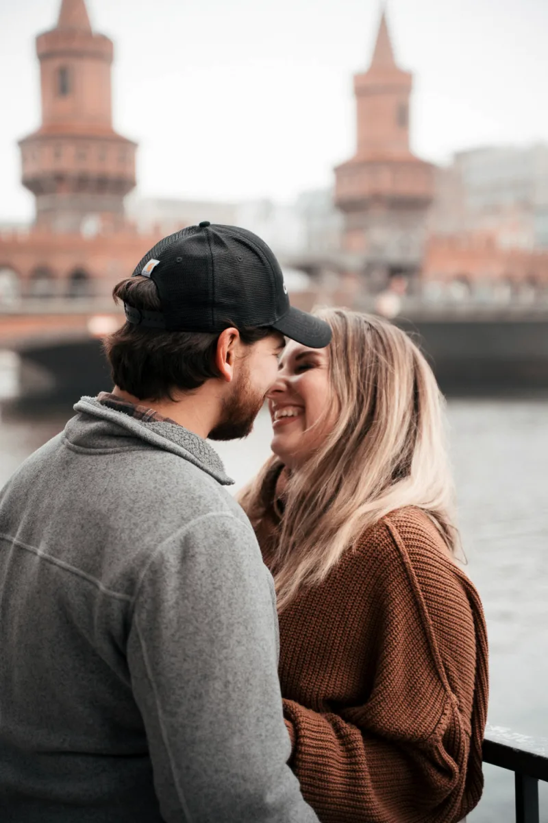 Couple smiling together by waterfront with blurred historic brick towers in background