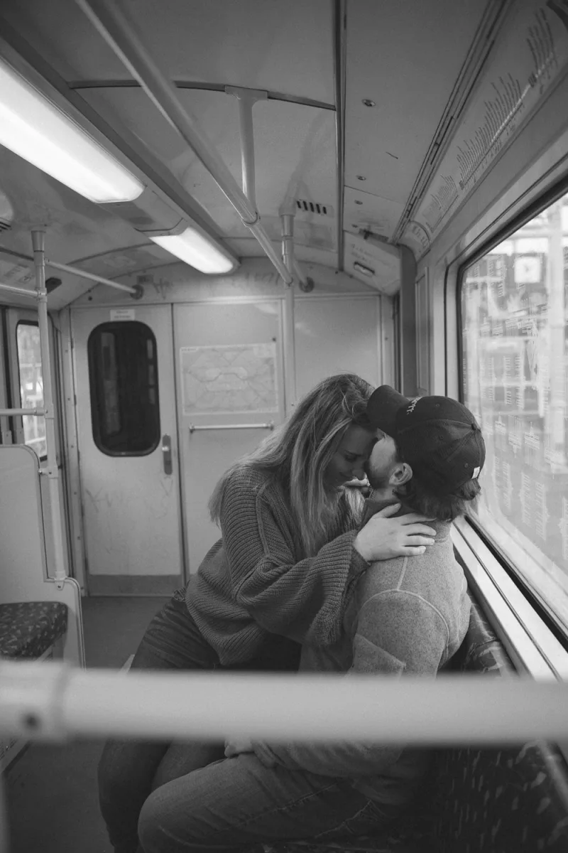 Black and white portrait of couple embracing on public transit train by window
