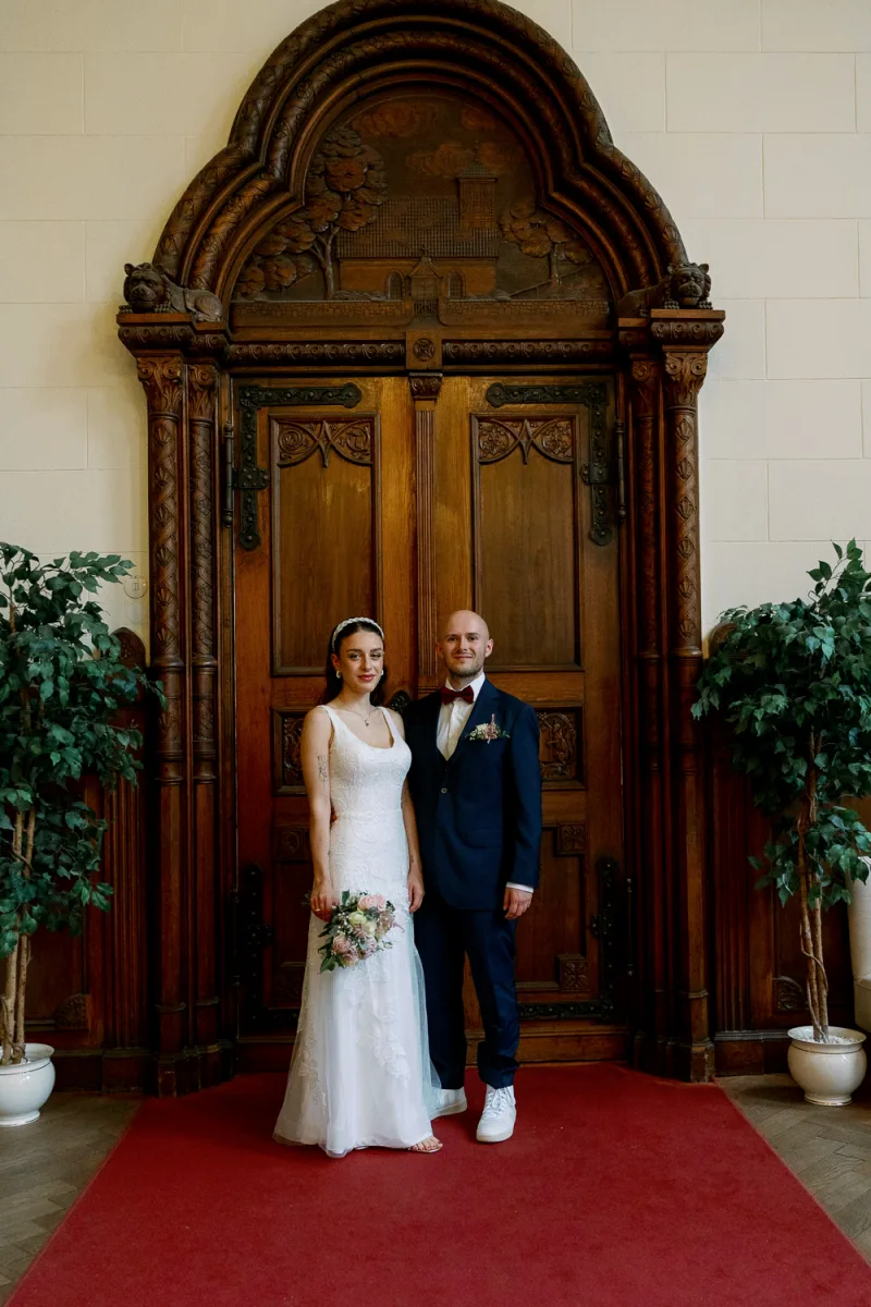 Bride in white lace gown and groom in navy suit at ornate doorway