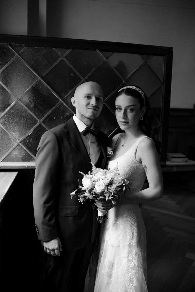 Bride in white lace and groom in formal attire with bouquet, black and white