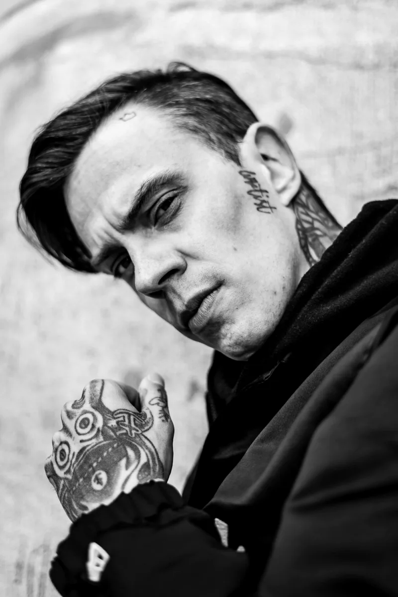 Young man with dark hair and head tattoo looking away pensively in sunlight