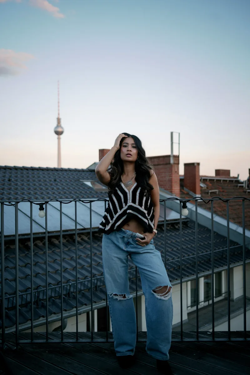 Woman on rooftop wearing striped top and ripped jeans at sunset with urban skyline
