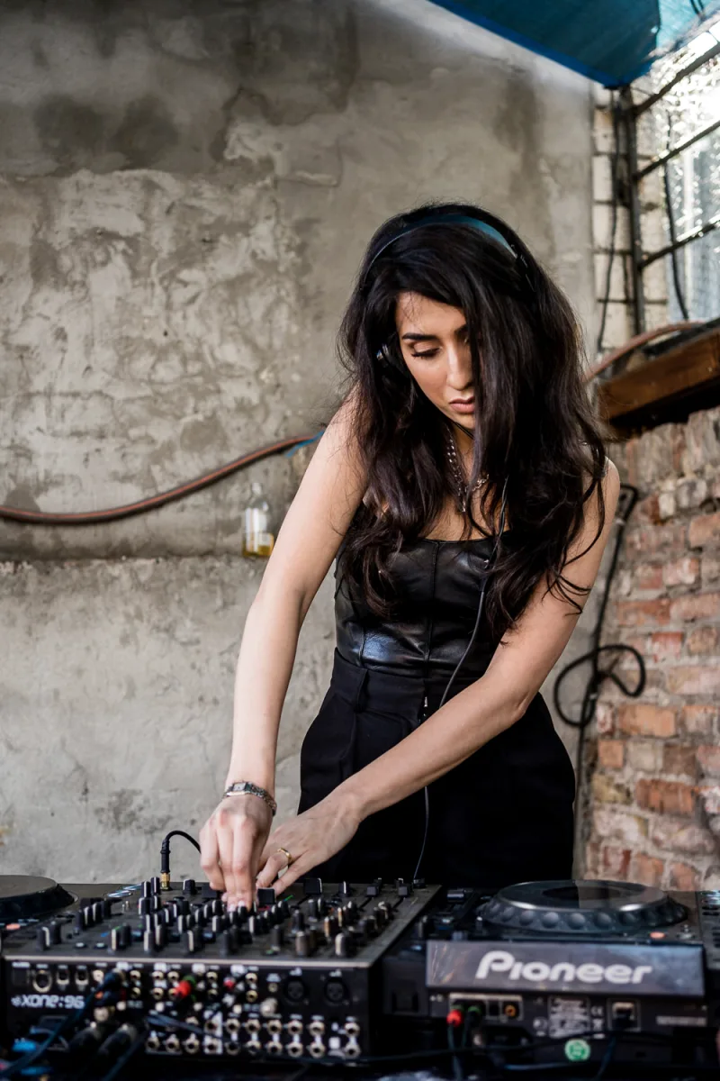 DJ woman in black attire operating mixing equipment in industrial concrete space