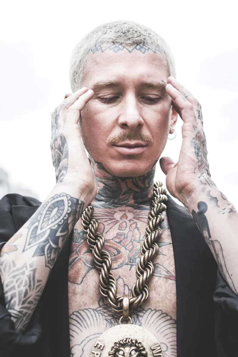 Tattooed man holding face with eyes closed and forehead tattoo against white