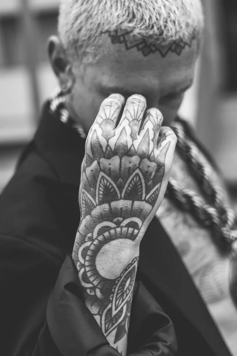 Person with white hair displaying ornate hand tattoo with floral designs
