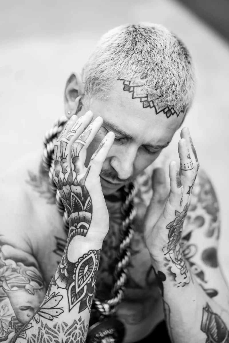 Tattooed man with shaved head framing his face with tattooed hands thoughtfully