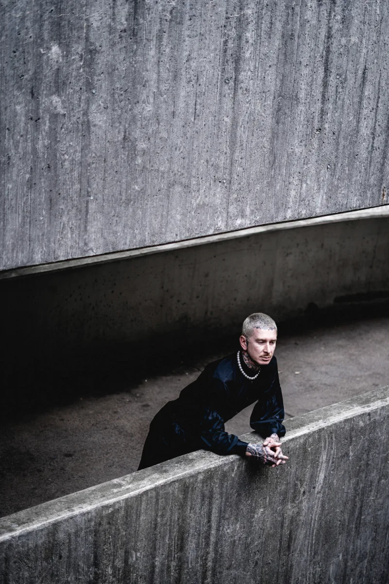 Man in dark velvet jacket and chain necklace in concrete underpass