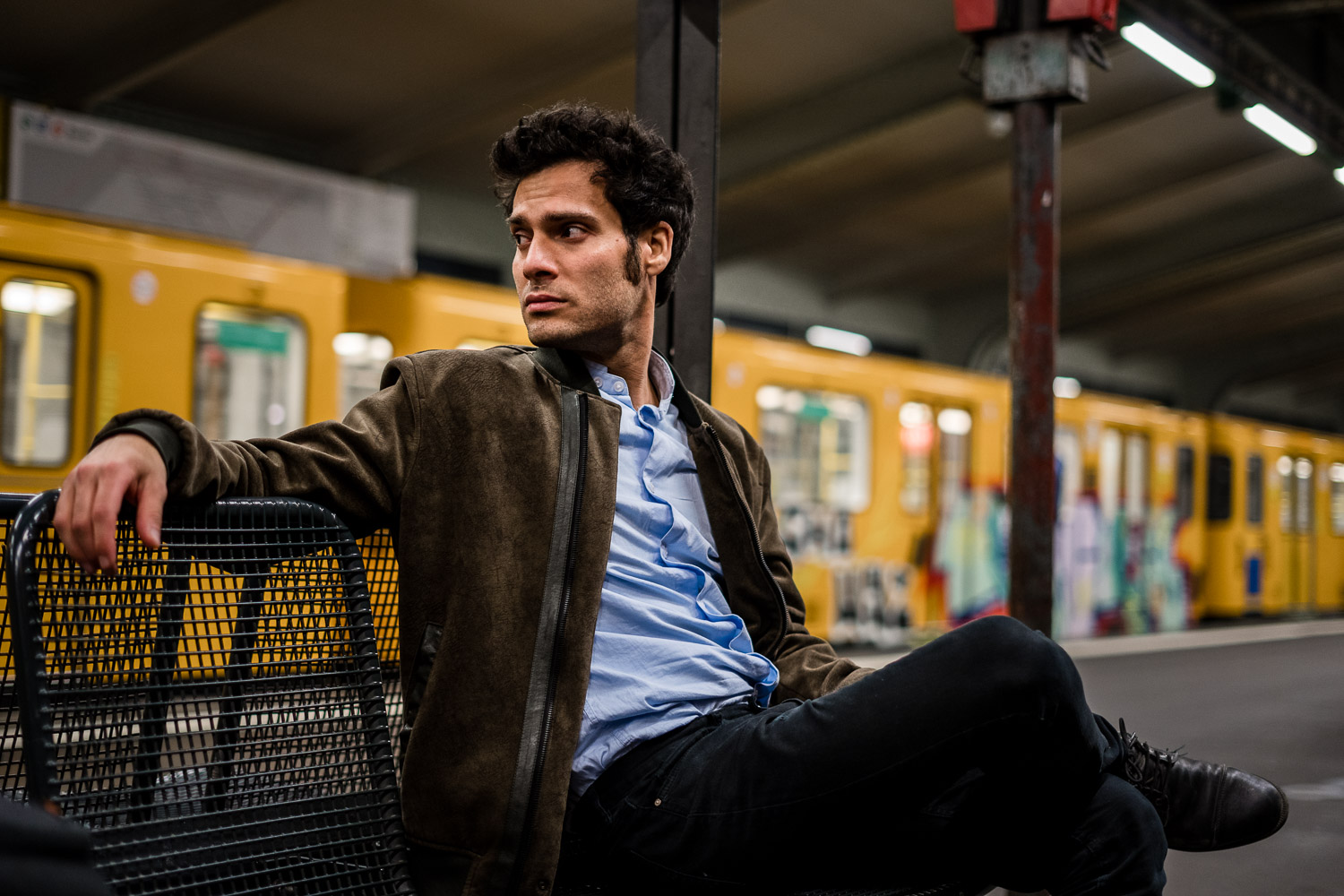 Man in brown jacket and blue shirt sitting on yellow metal crate