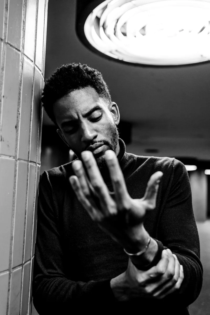 Man with hand to face leaning against wall in contemplative black and white portrait