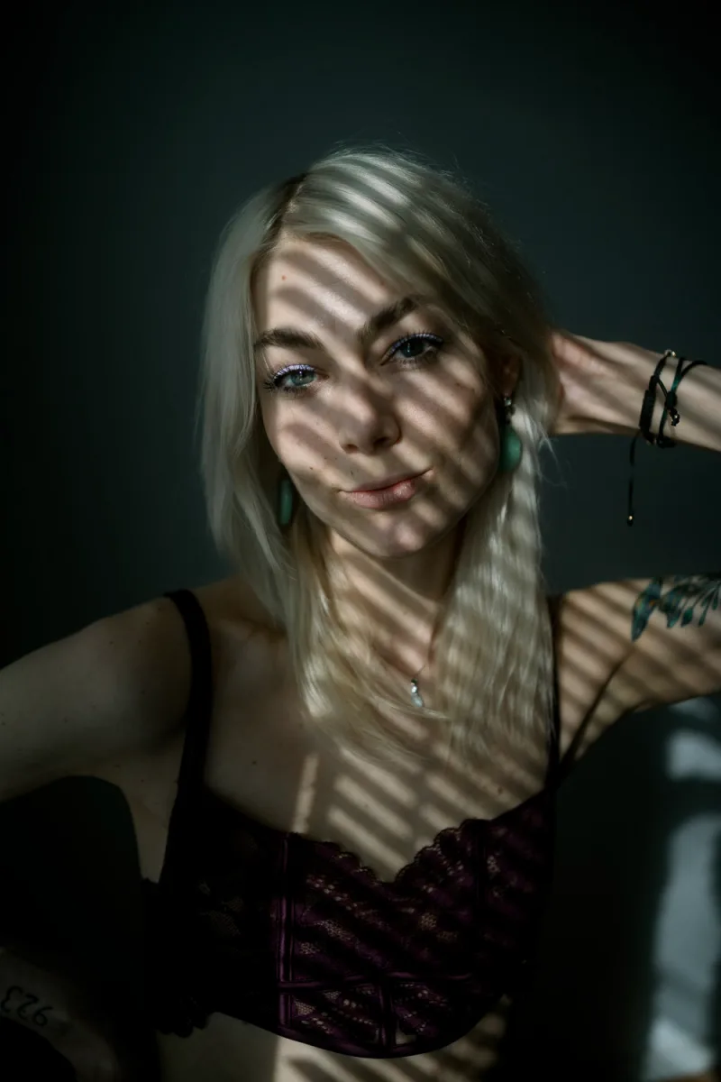 Woman with light hair in dark moody portrait with shadowed face patterns visible