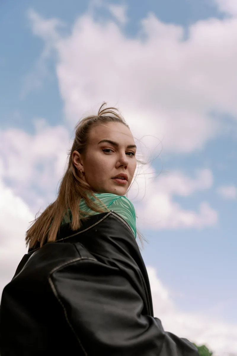 Blonde woman wearing green scarf against cloudy sky backdrop, looking aside