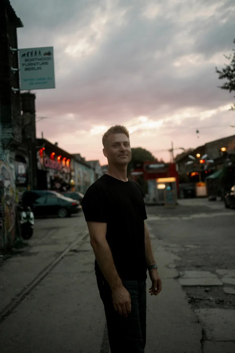 Man in black shirt standing on dusk urban street with storefront and vintage sign